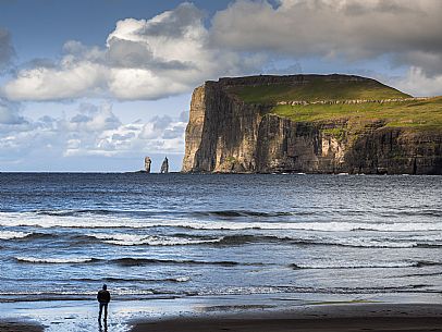 Tourist in the Tjrnuvk beach, Streymoy island. On the horizon, the silhouettes of Risin and  Kellingin sea stacks, Faeroe islands, Denmark, Europe